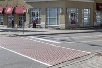 some cars parked at a red light and some people walking by it and buildings with awnings