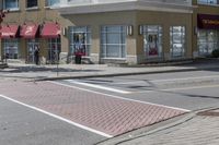 some cars parked at a red light and some people walking by it and buildings with awnings