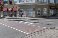 some cars parked at a red light and some people walking by it and buildings with awnings