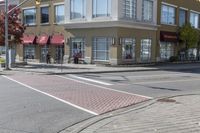 some cars parked at a red light and some people walking by it and buildings with awnings