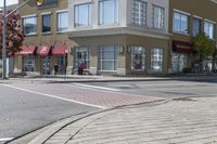 some cars parked at a red light and some people walking by it and buildings with awnings