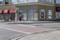 some cars parked at a red light and some people walking by it and buildings with awnings