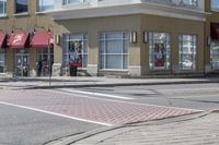 some cars parked at a red light and some people walking by it and buildings with awnings