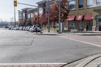 some cars parked at a red light and some people walking by it and buildings with awnings