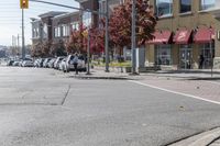 some cars parked at a red light and some people walking by it and buildings with awnings