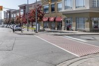 some cars parked at a red light and some people walking by it and buildings with awnings