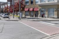 some cars parked at a red light and some people walking by it and buildings with awnings