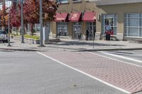 some cars parked at a red light and some people walking by it and buildings with awnings