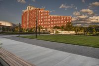 a city street surrounded by grass and tall buildings at the end of a street there is a paved pathway in front of the building