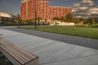 a city street surrounded by grass and tall buildings at the end of a street there is a paved pathway in front of the building