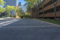 a paved area surrounded by tall buildings and trees with leaves on them, a paved road with a few benches and trees