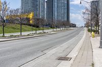 there is an empty street along the street with tall buildings behind it and trees lining the curb