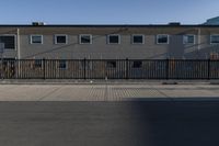 a fence near a building and street that has no cars on it, there is a clock and traffic