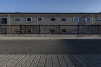 a fence near a building and street that has no cars on it, there is a clock and traffic