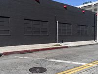 a traffic light on the side of a black building next to an empty street with a manholed road and red lights