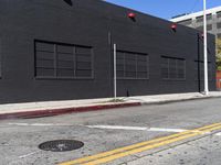 a traffic light on the side of a black building next to an empty street with a manholed road and red lights