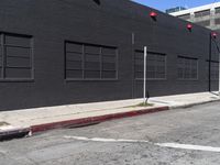 a traffic light on the side of a black building next to an empty street with a manholed road and red lights