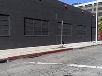 a traffic light on the side of a black building next to an empty street with a manholed road and red lights