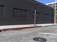 a traffic light on the side of a black building next to an empty street with a manholed road and red lights