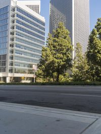 a man riding a bicycle on the side of a road next to tall buildings and trees