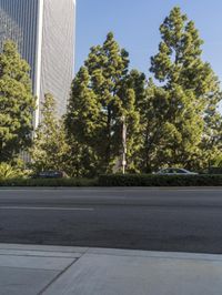 a man riding a bicycle on the side of a road next to tall buildings and trees