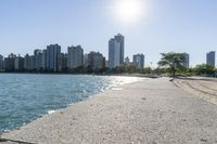 two people walk along a walkway by the water in front of city buildings and a body of