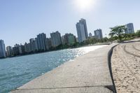 two people walk along a walkway by the water in front of city buildings and a body of