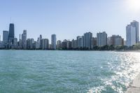 two people walk along a walkway by the water in front of city buildings and a body of