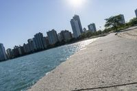 two people walk along a walkway by the water in front of city buildings and a body of