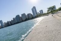 two people walk along a walkway by the water in front of city buildings and a body of