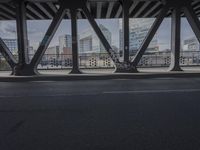 the view from underneath a bridge at an intersection with the skyline visible behind it and a vehicle going under the pedestrian bridge