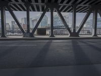 the view from underneath a bridge at an intersection with the skyline visible behind it and a vehicle going under the pedestrian bridge