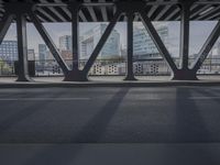 the view from underneath a bridge at an intersection with the skyline visible behind it and a vehicle going under the pedestrian bridge