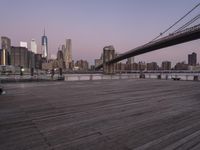 a park bench and benches on the boardwalk with a view of the city skyline and bridge