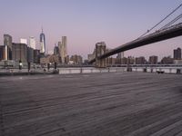 a park bench and benches on the boardwalk with a view of the city skyline and bridge