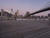 a park bench and benches on the boardwalk with a view of the city skyline and bridge