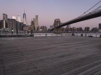 a park bench and benches on the boardwalk with a view of the city skyline and bridge