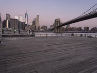 a park bench and benches on the boardwalk with a view of the city skyline and bridge