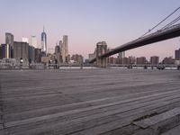 a park bench and benches on the boardwalk with a view of the city skyline and bridge