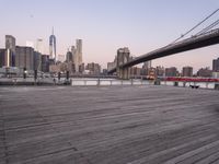 a park bench and benches on the boardwalk with a view of the city skyline and bridge