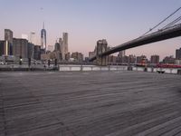 a park bench and benches on the boardwalk with a view of the city skyline and bridge