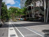 an image of a street that is surrounded by trees and buildings in the background there are two trees next to the road