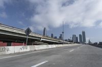 a view of city from inside of a vehicle in a moving blurry picture, including the roof of the vehicle and a sign on the side of the freeway that reads under