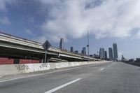 a view of city from inside of a vehicle in a moving blurry picture, including the roof of the vehicle and a sign on the side of the freeway that reads under