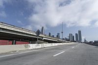 a view of city from inside of a vehicle in a moving blurry picture, including the roof of the vehicle and a sign on the side of the freeway that reads under