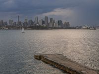 an empty bench is overlooking a large city on the water and on a cloudy day