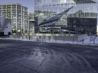 large glass buildings on the side of a road in the city with snowy ground and bushes behind them