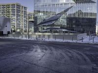 large glass buildings on the side of a road in the city with snowy ground and bushes behind them