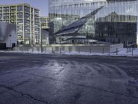 large glass buildings on the side of a road in the city with snowy ground and bushes behind them