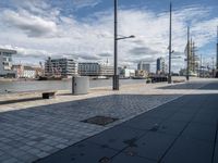 there is a bench on this sidewalk by the water next to buildings and boats in the background